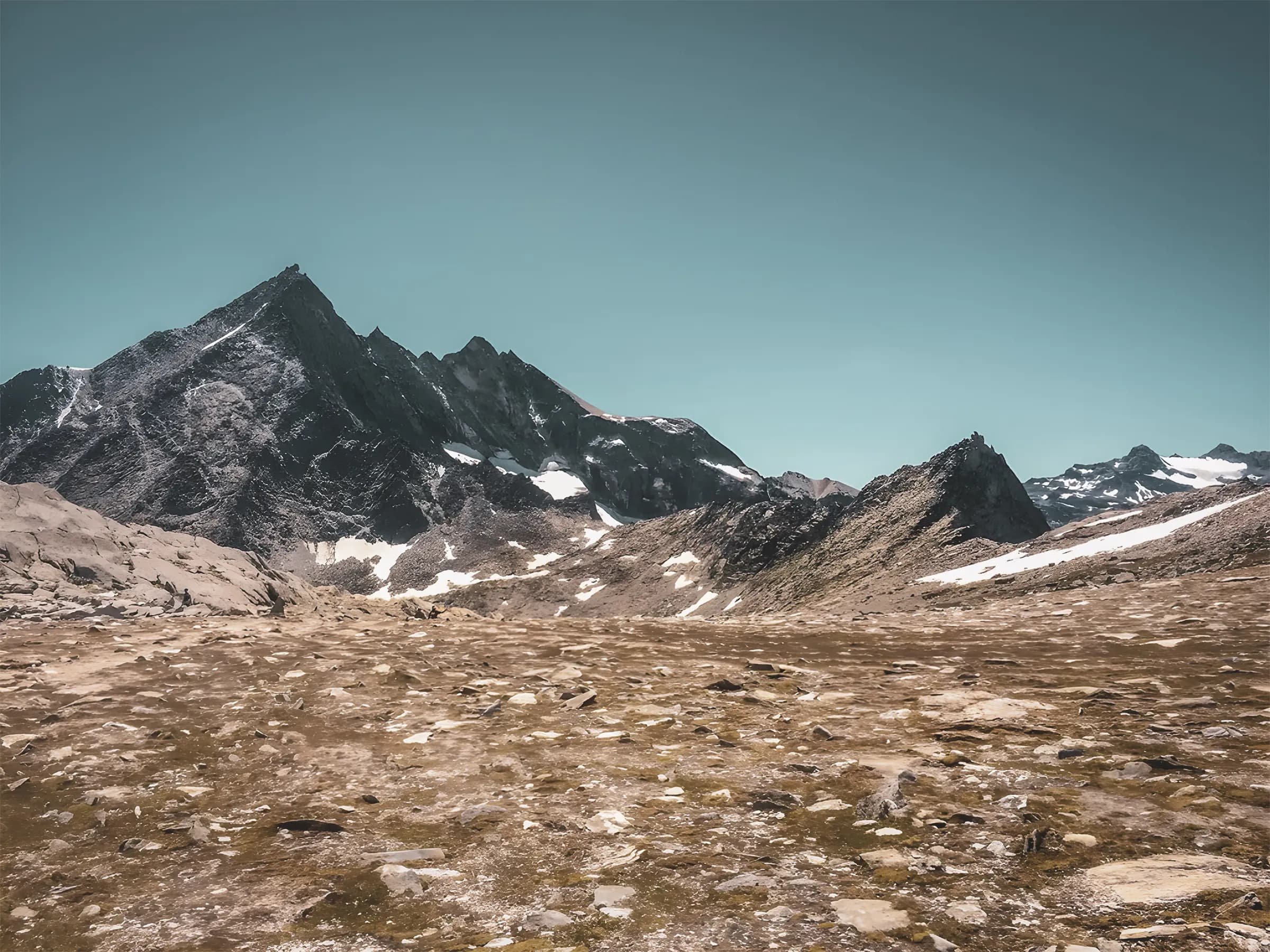 Majestic Alpine scenery with craggy peaks and vast meadows under a clear blue sky.