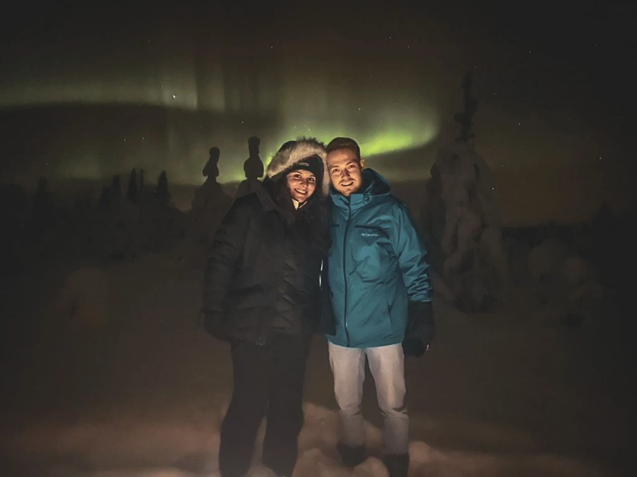 Two smiling people under the northern lights, surrounded by snow in Lapland.