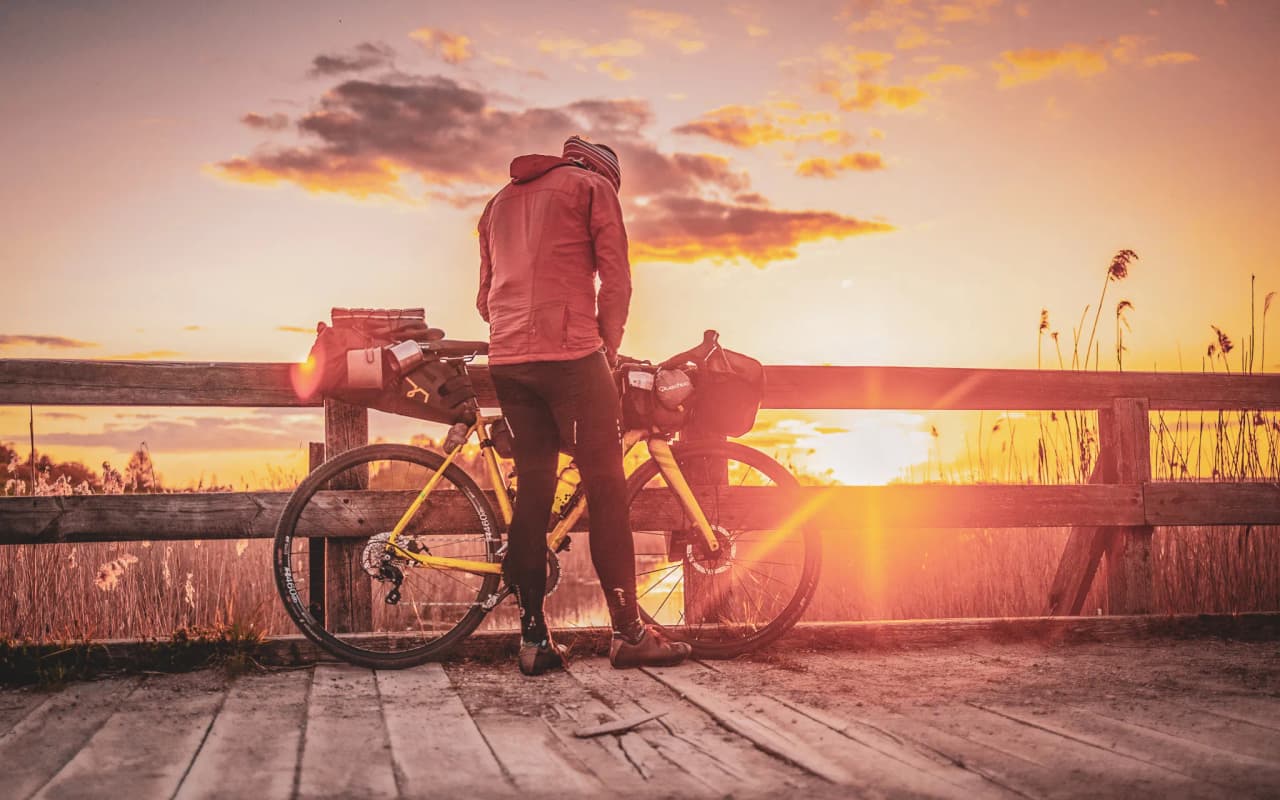 A cyclist admiring a golden sunset, surrounded by peaceful forest landscapes.