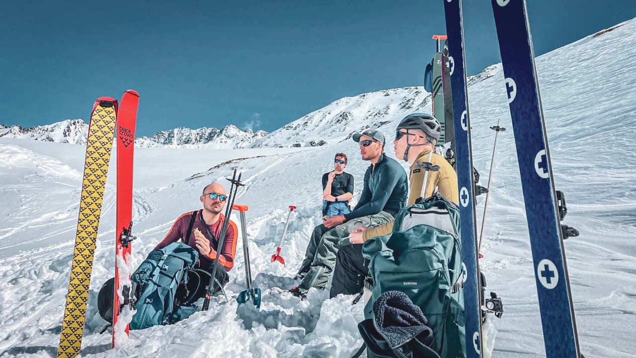A group of adventurers taking a break, skis planted in the snow, under a brilliant blue sky.