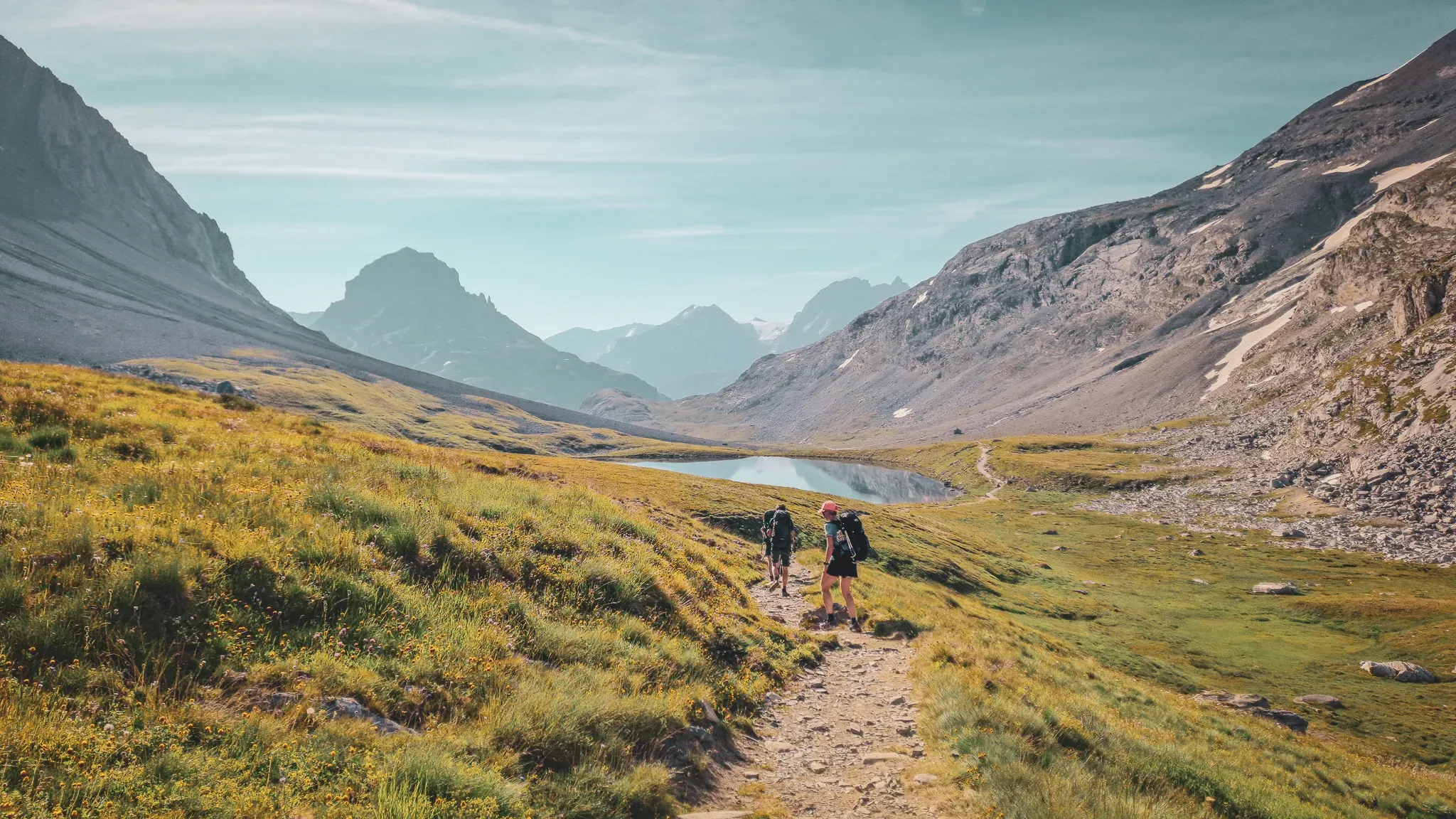 Hikers on their way to a high-altitude lake, surrounded by majestic peaks and flower-filled meadows.