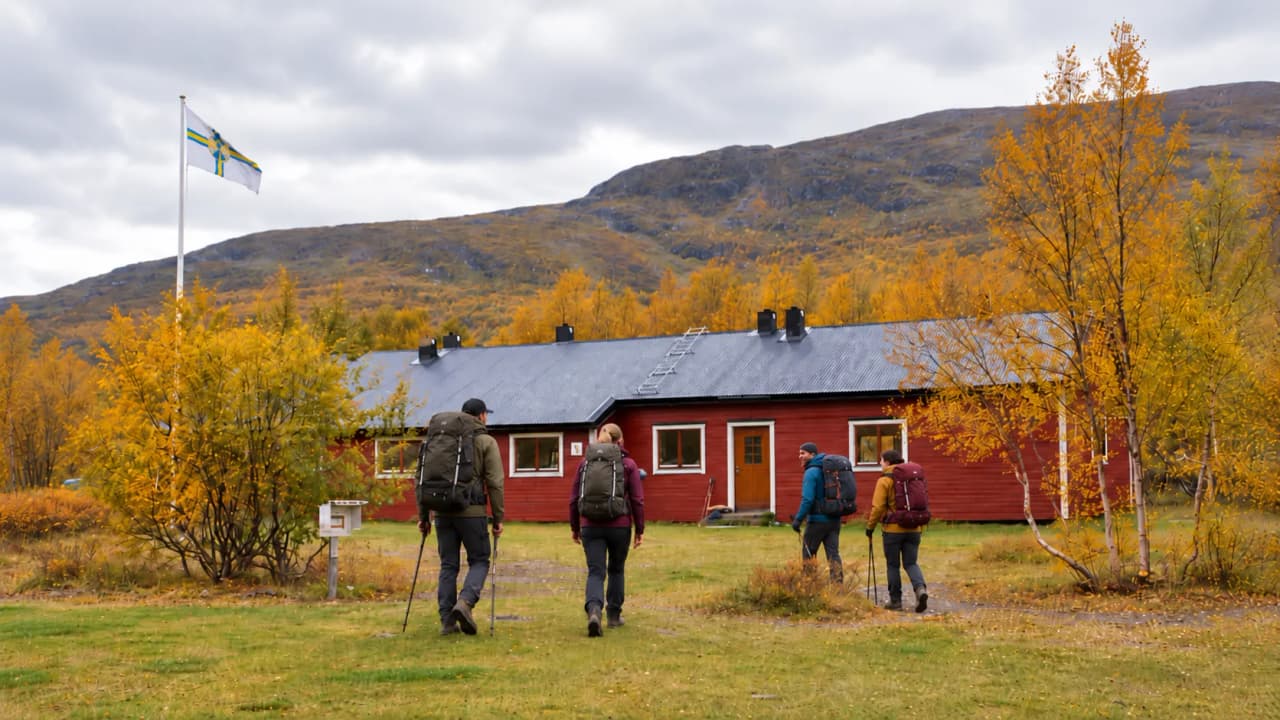 Groupe de randonneurs en Laponie, cheminant vers un chalet rouge sous un ciel nuageux.