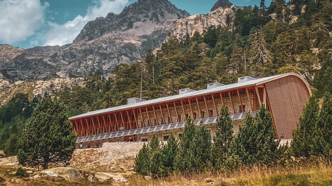 Refuge moderne niché entre montagnes majestueuses, entouré de verdure et d'aventures.