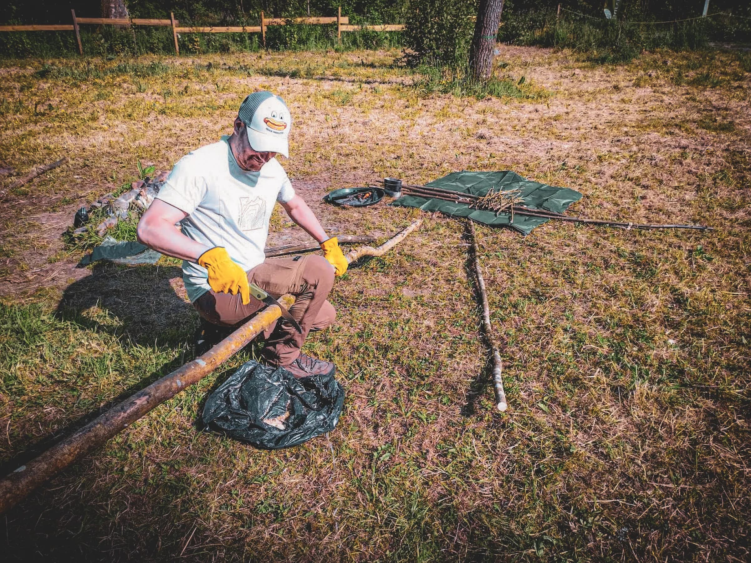 Un participant en stage de survie sculpte un bâton dans la verdure ensoleillée de l'Ardenne belge.