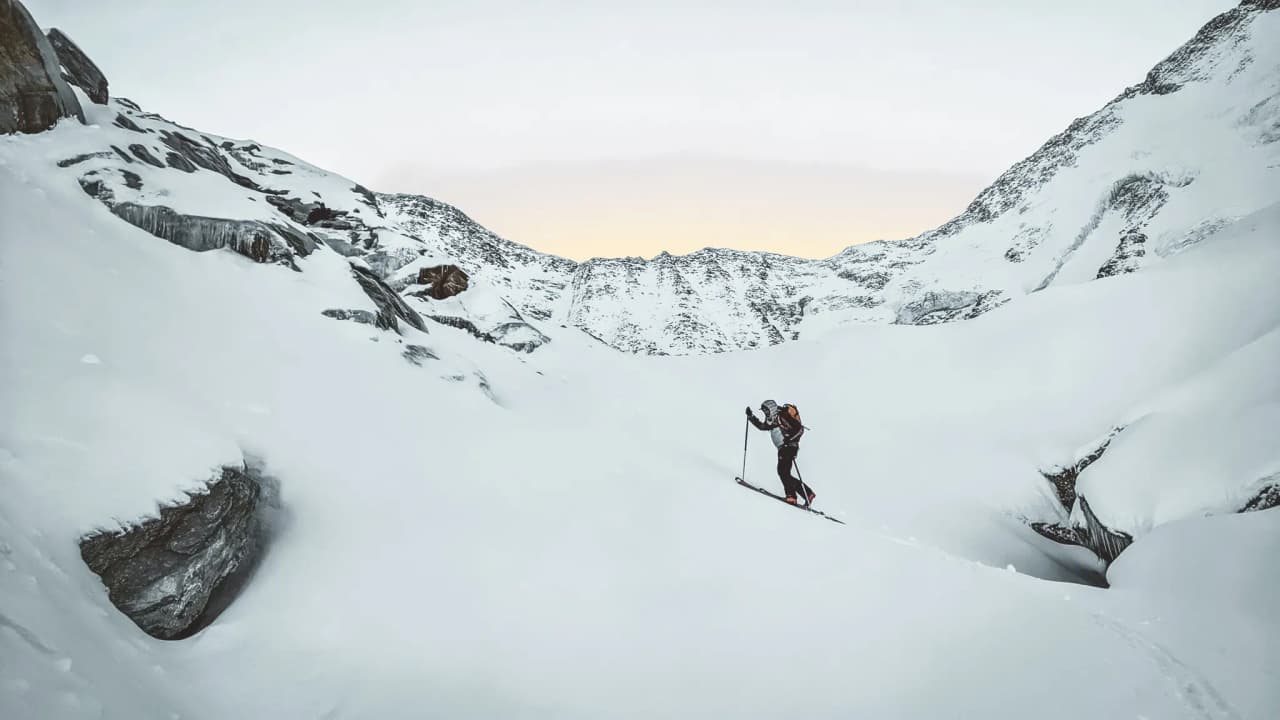 A ski tourer crosses a majestic snow-covered landscape, surrounded by impressive mountains.