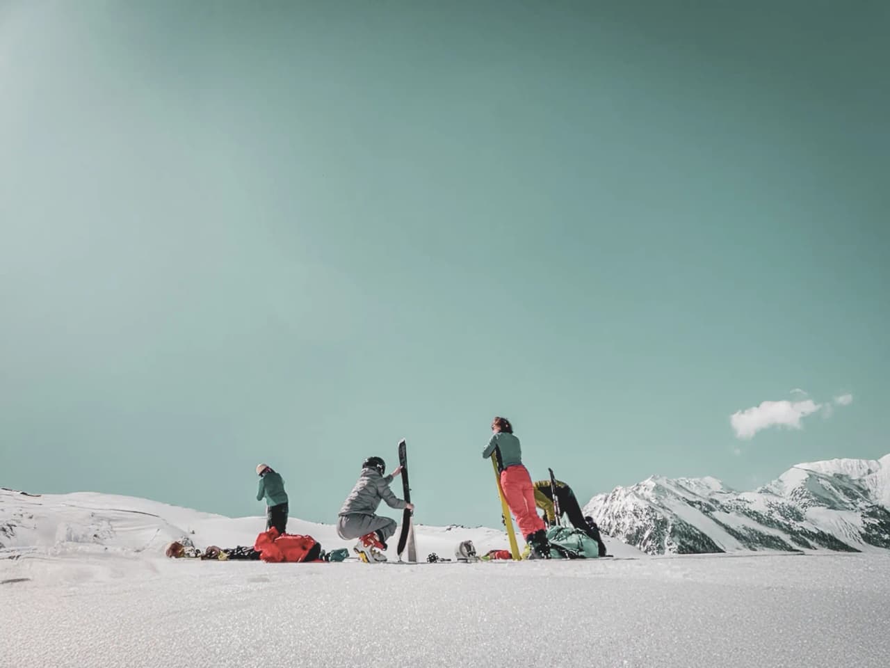 Group of skiers on a vast glacier, mountains in the background, blue sky and light clouds.