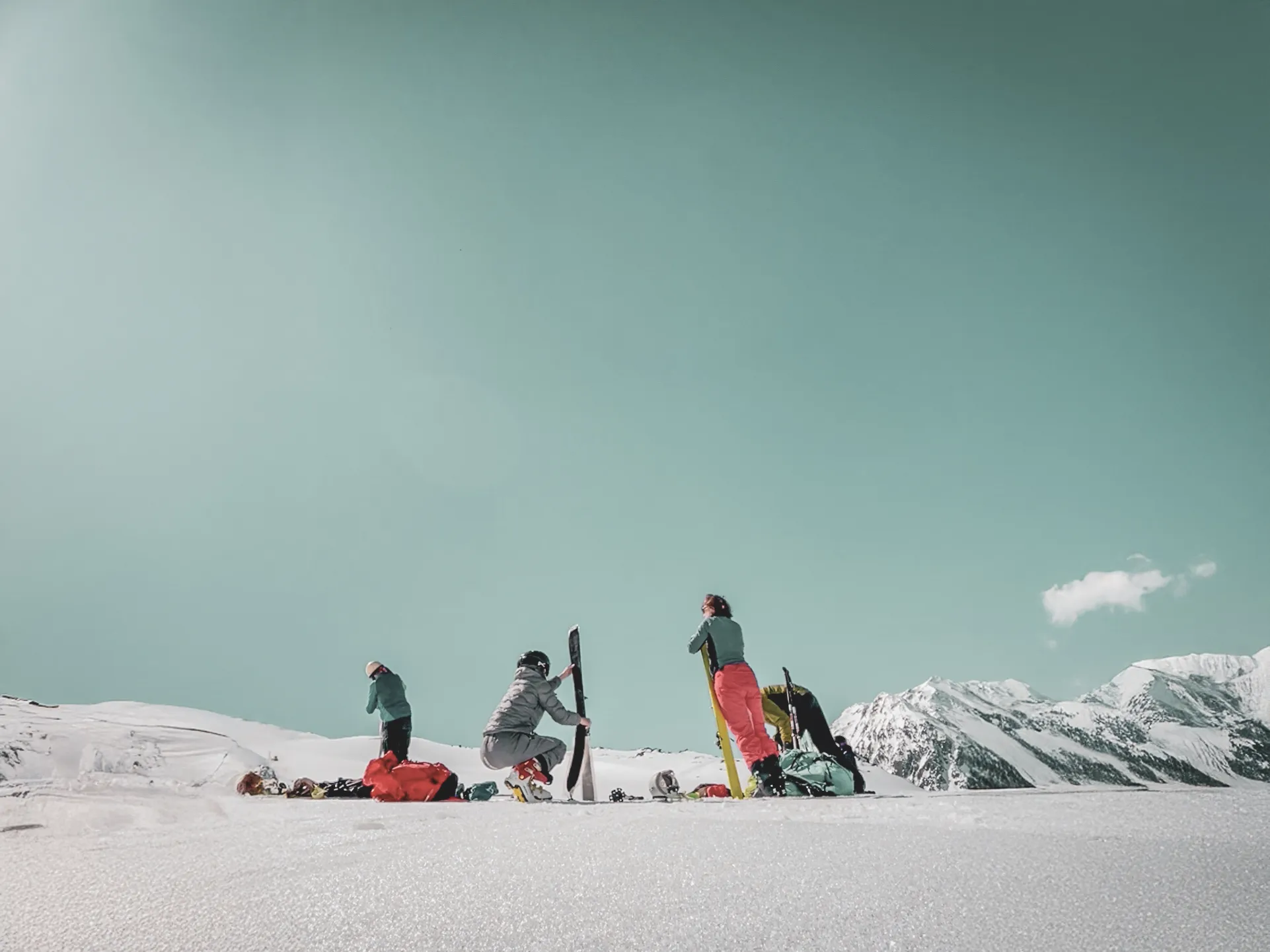 Group of skiers on a vast glacier, mountains in the background, blue sky and light clouds.