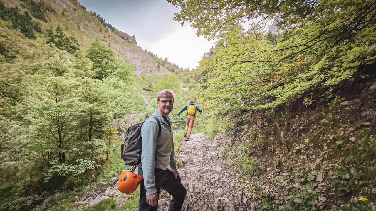 Two smiling hikers on a lush green path leading to Mont Aiguille, surrounded by nature.