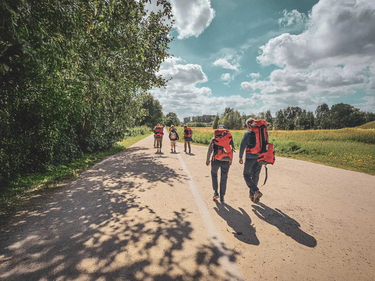 Groupe de randonneurs en packraft marchant sur un chemin, entouré de verdure et de ciel bleu.