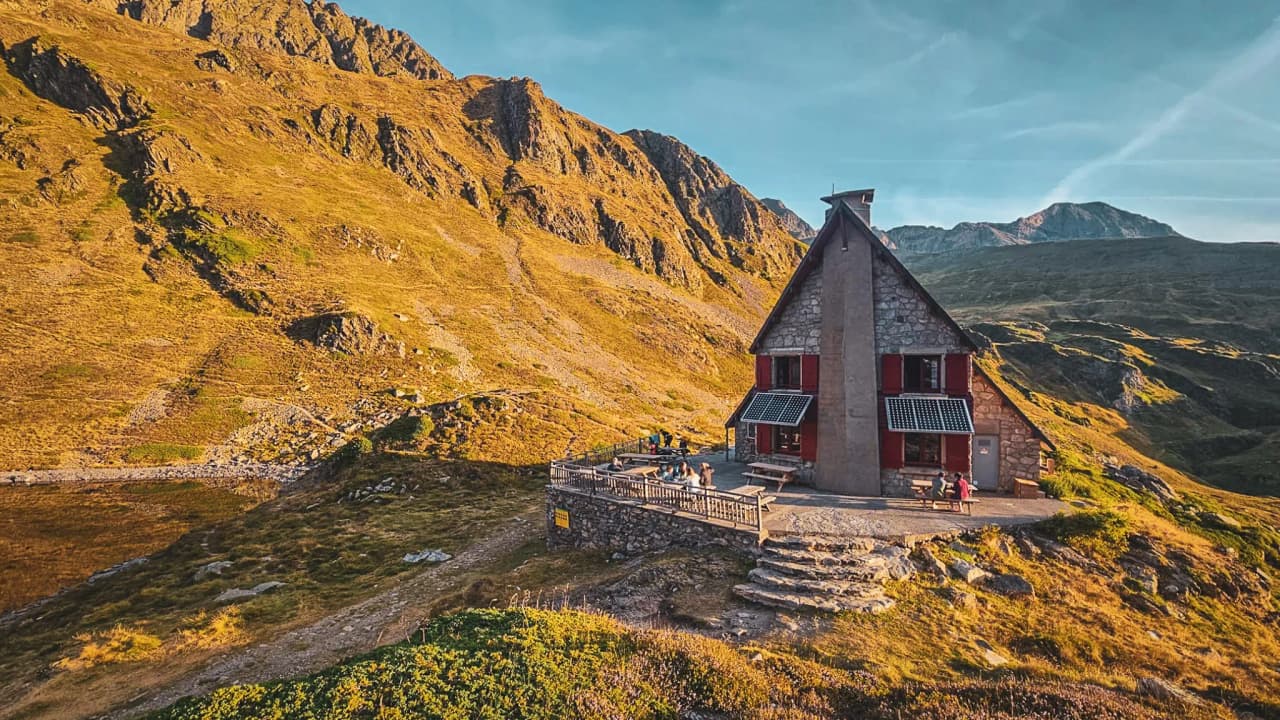 Refuge de montagne pittoresque sous un ciel bleu azur, entouré de vallées dorées et impressionnantes.