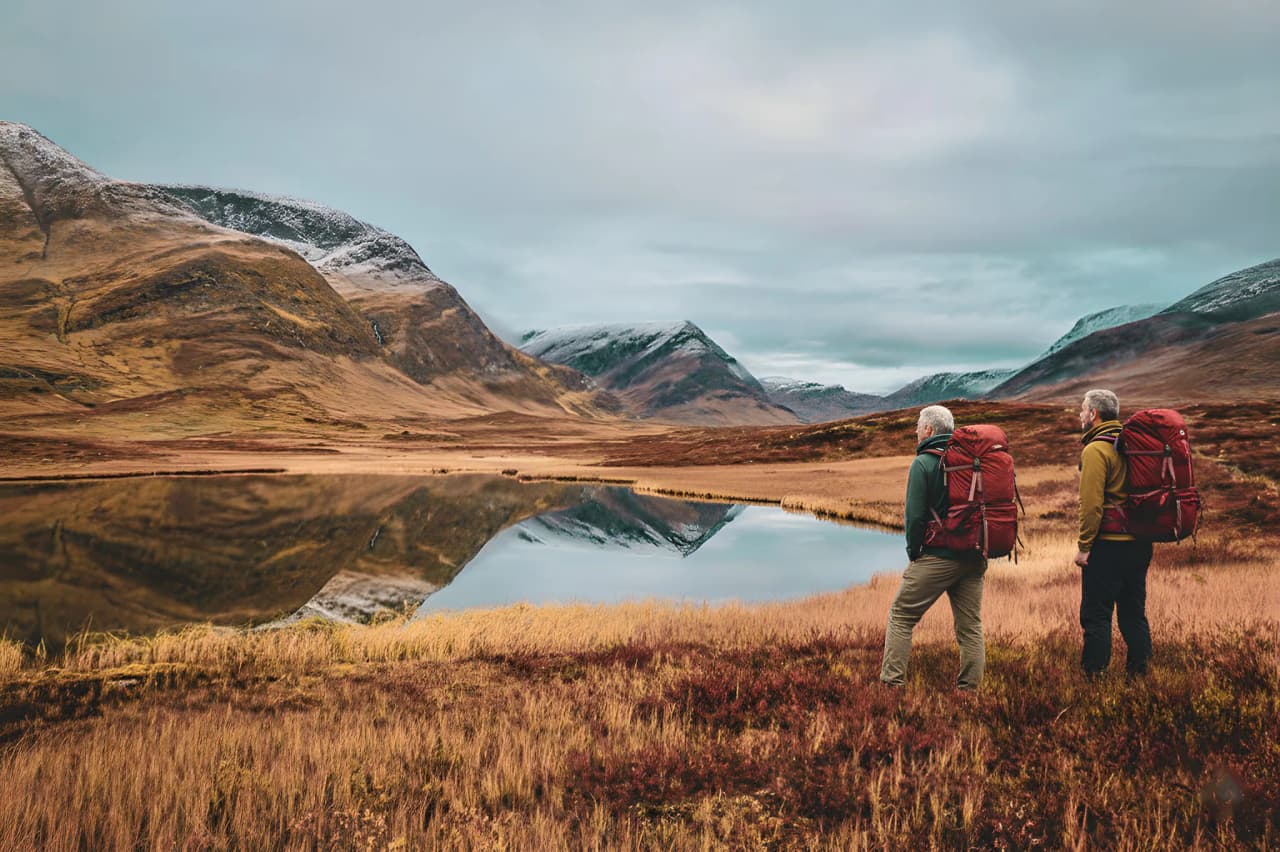 Deux randonneurs contemplent un paysage montagneux miroir dans un environnement sauvage et paisible.