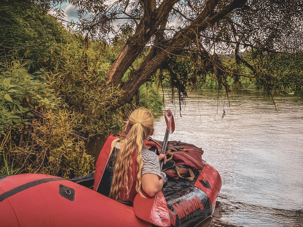 Une personne sur un packraft explore une paisible rivière bordée de verdure luxuriante.