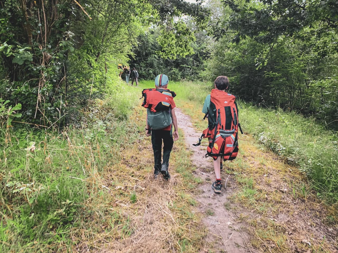 Deux jeunes aventuriers marchent sur un sentier verdoyant, prêts à explorer la nature belge.