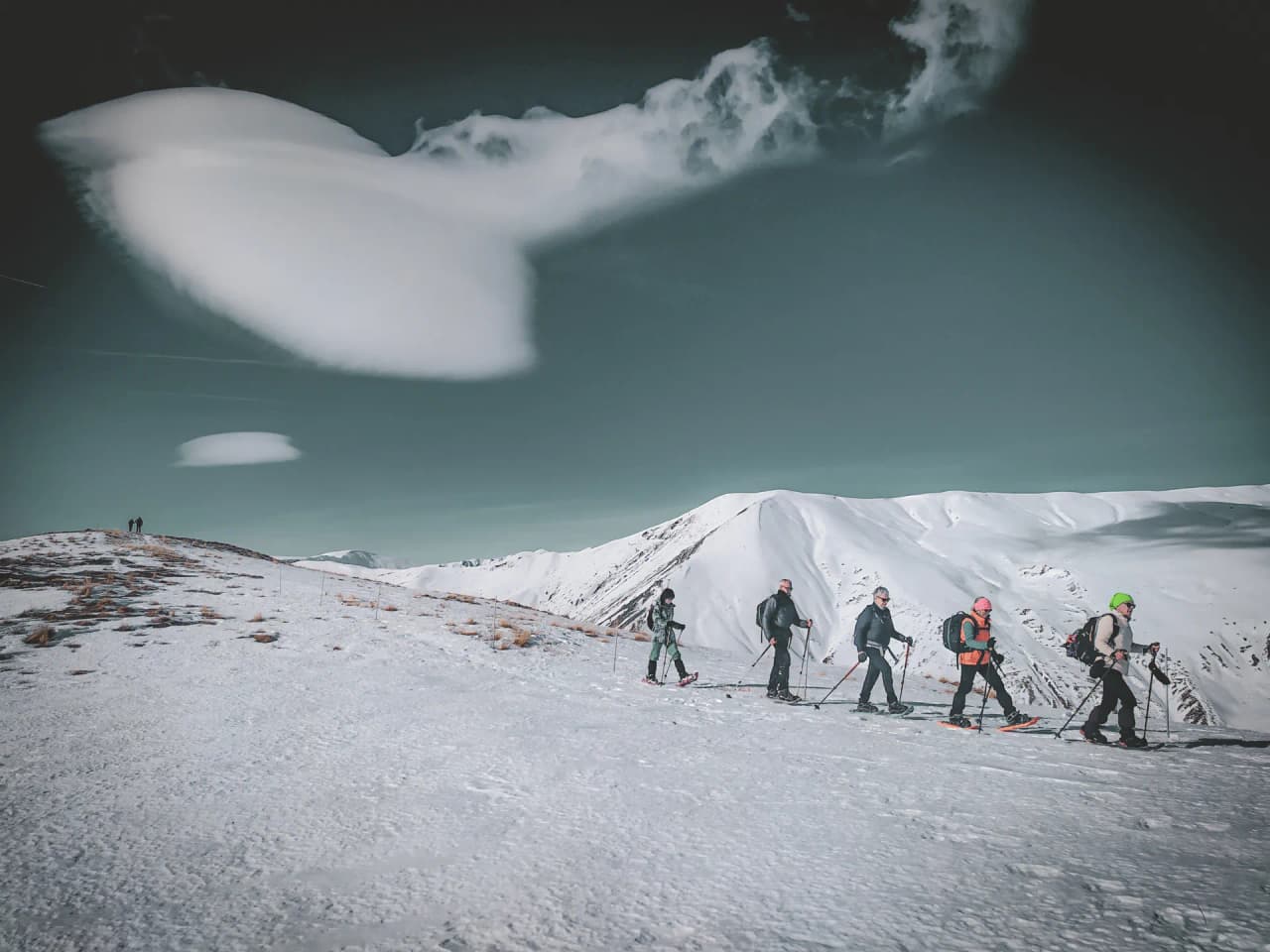 A group of explorers on snowshoes make their way across a magical, snow-covered alpine landscape.