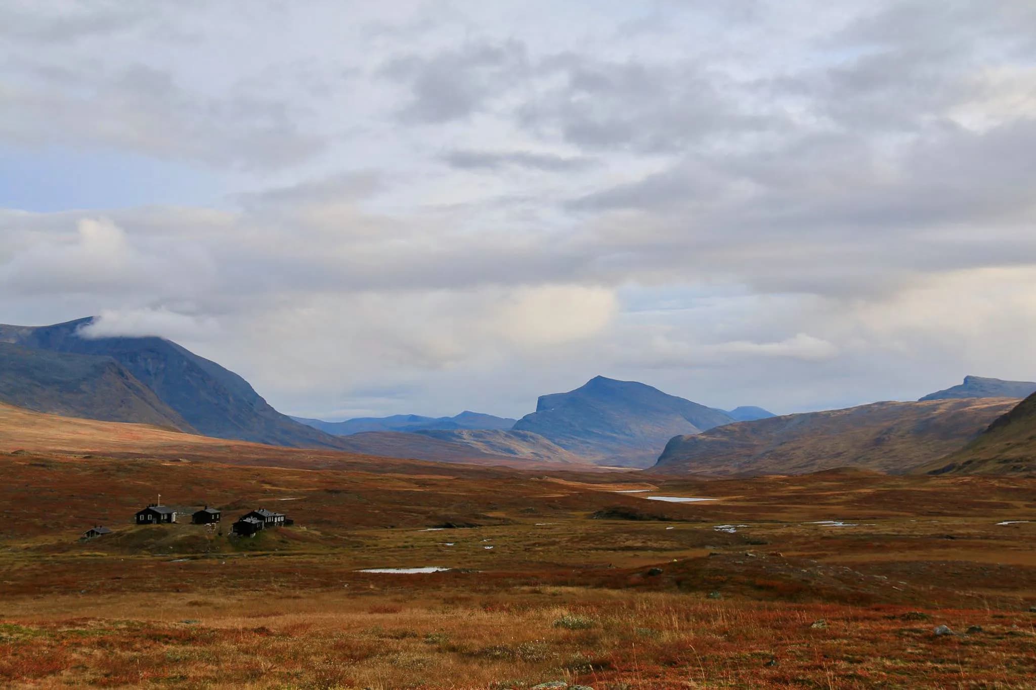 Un vaste paysage de collines ondulées en Laponie Suédoise près de Abisko. Des vallées profondes et un ciel nuageux overhead. Au premier plan, une étendue de terrain aux teintes dorées et brunes.