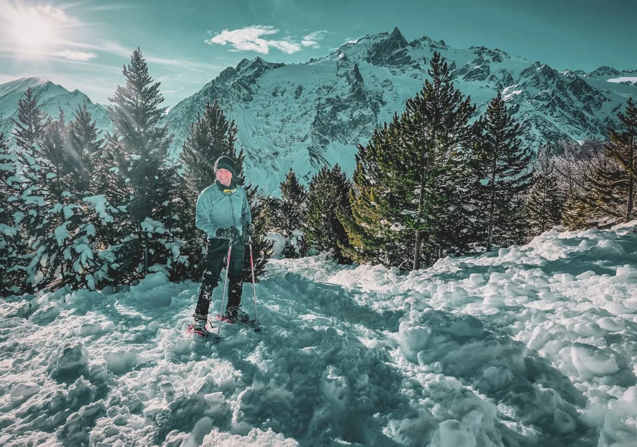 A man on snowshoes smiling in a snow-covered landscape with majestic mountains in the background.