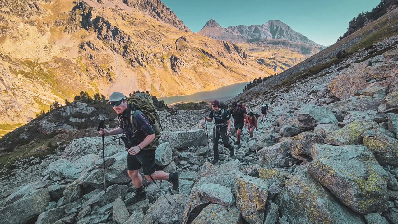 Groupe de randonneurs gravissant des rochers avec des paysages montagneux et un lac en toile de fond.