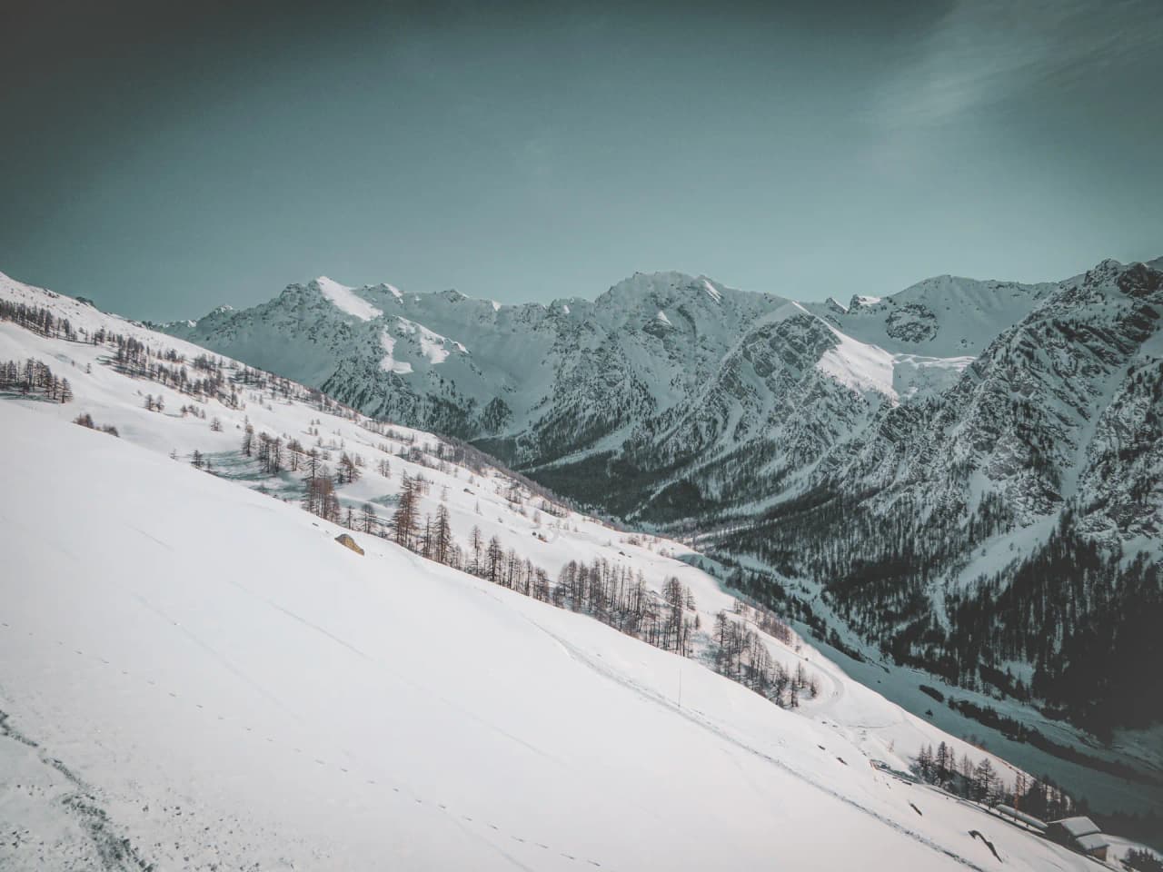 Snow-covered Alpine scenery, majestic valleys and mountains under clear skies, an invitation to adventure.