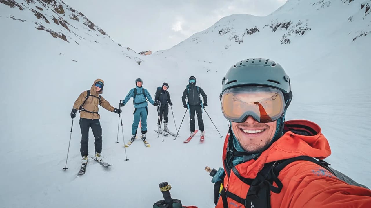 A group of smiling skiers in a snow-covered Alpine setting on the Great Saint Bernard Pass.