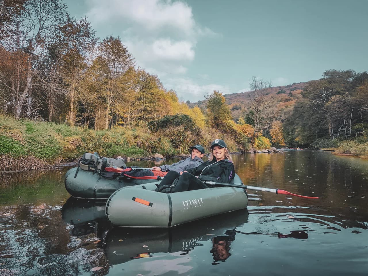 Deux personnes profitent d'une balade en packraft sur une rivière bordée d'arbres colorés en automne.