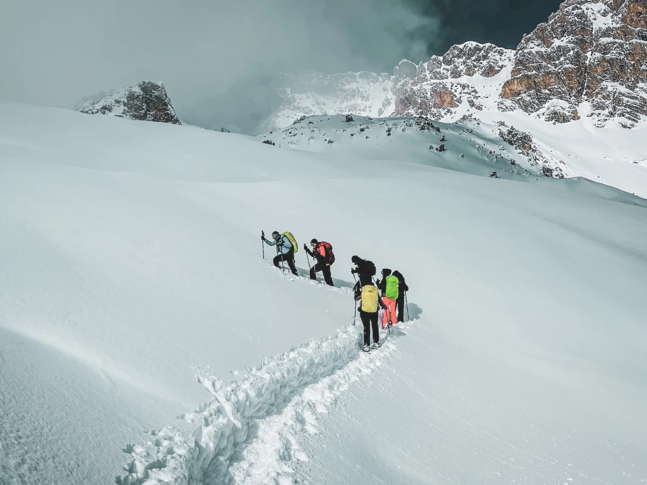 A group of hikers on snowshoes in a snow-covered landscape, with the Meije in the background.