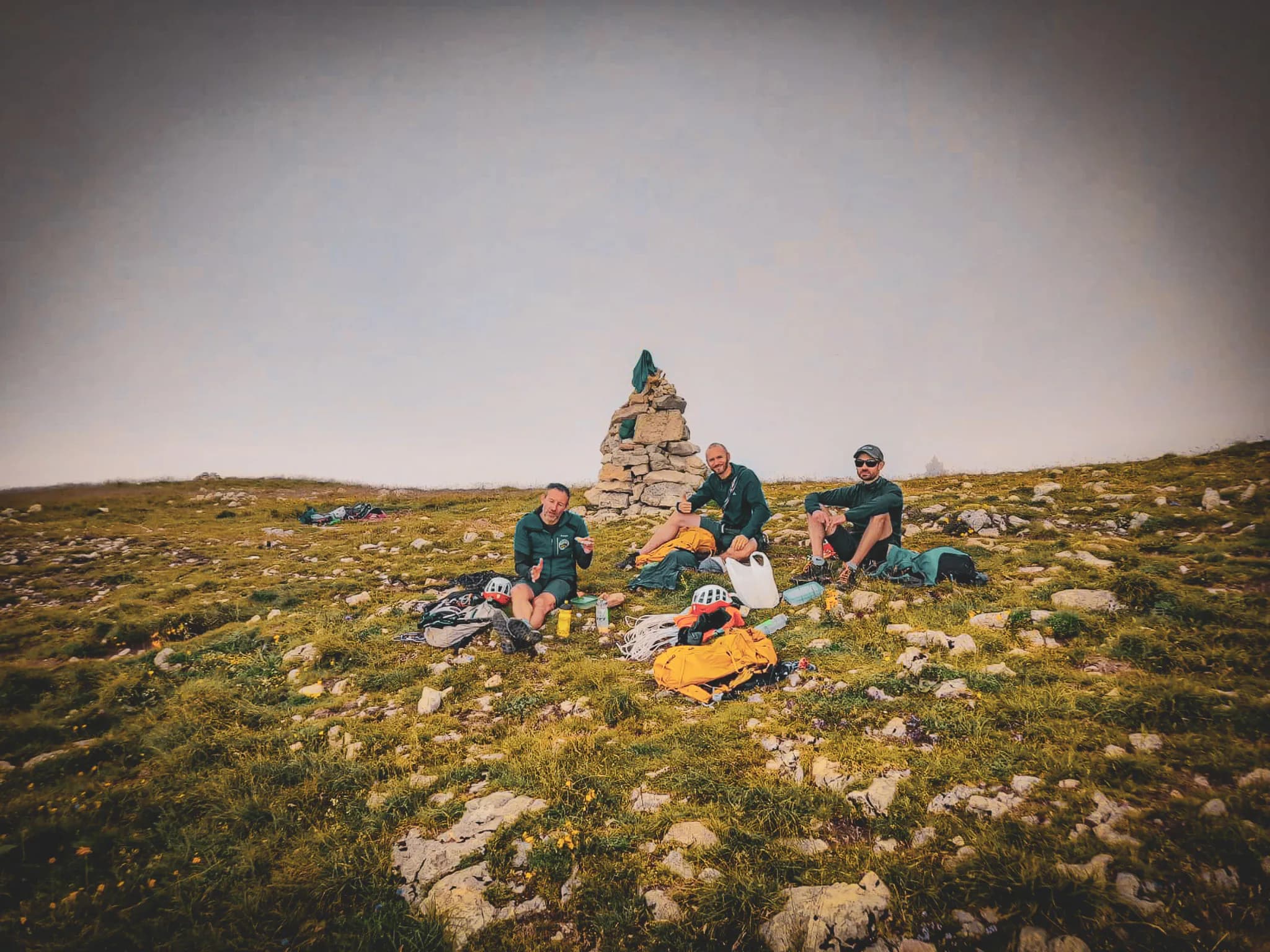 Three relaxed climbers on a green summit, admiring the view of Mont Aiguille.
