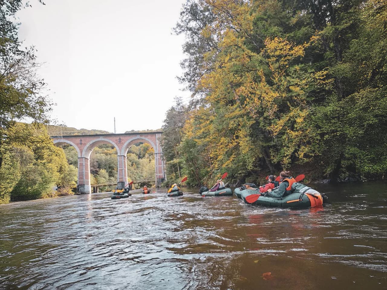 Groupe de packrafts naviguant paisiblement sous un viaduc, au cœur des forêts d'Ardenne.