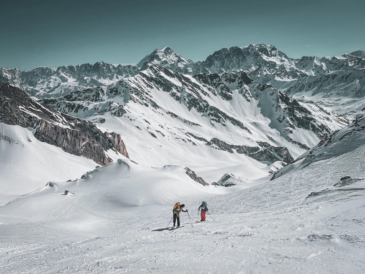 Two skiers on a hike in a snow-covered Alpine landscape, surrounded by majestic mountains.