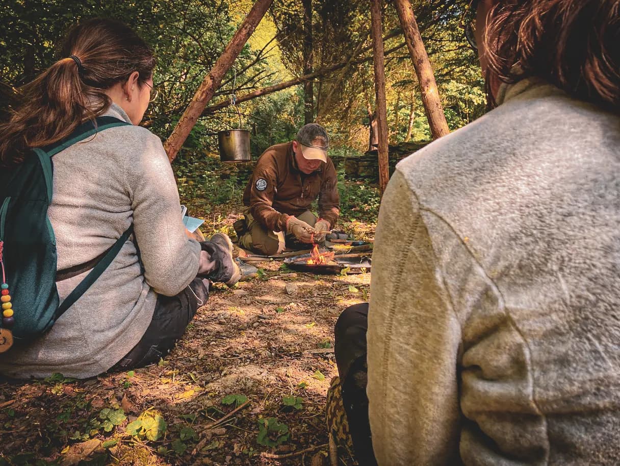 Groupe en pleine nature, apprenant la survie autour d'un feu, ambiance sereine en Ardenne.
