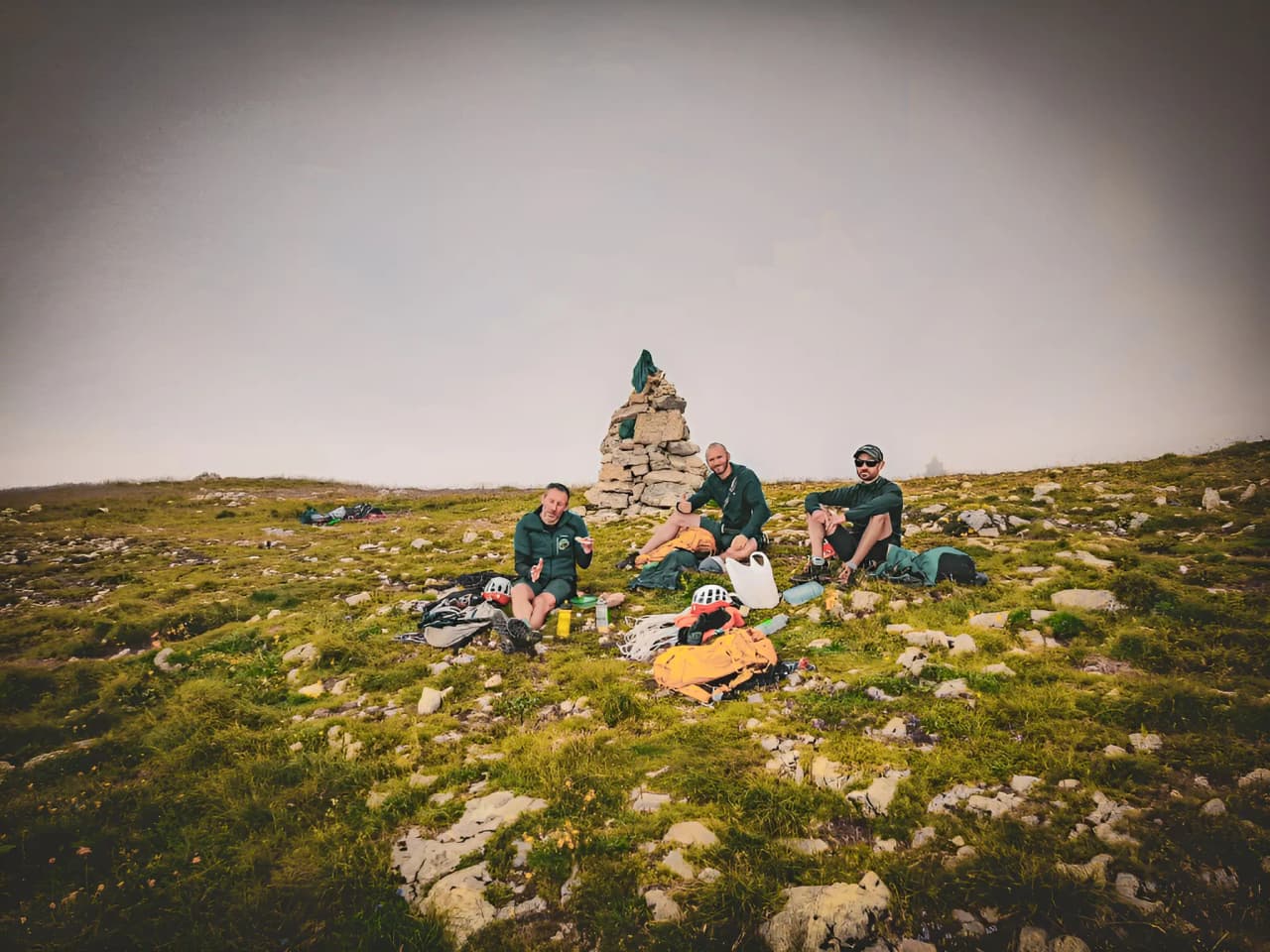 Three adventurers rest on Mont Aiguille, surrounded by greenery and majestic scenery.