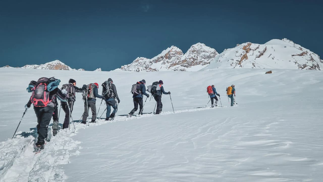 Group of hikers on snowshoes, immaculate snow, majestic mountains in the background.