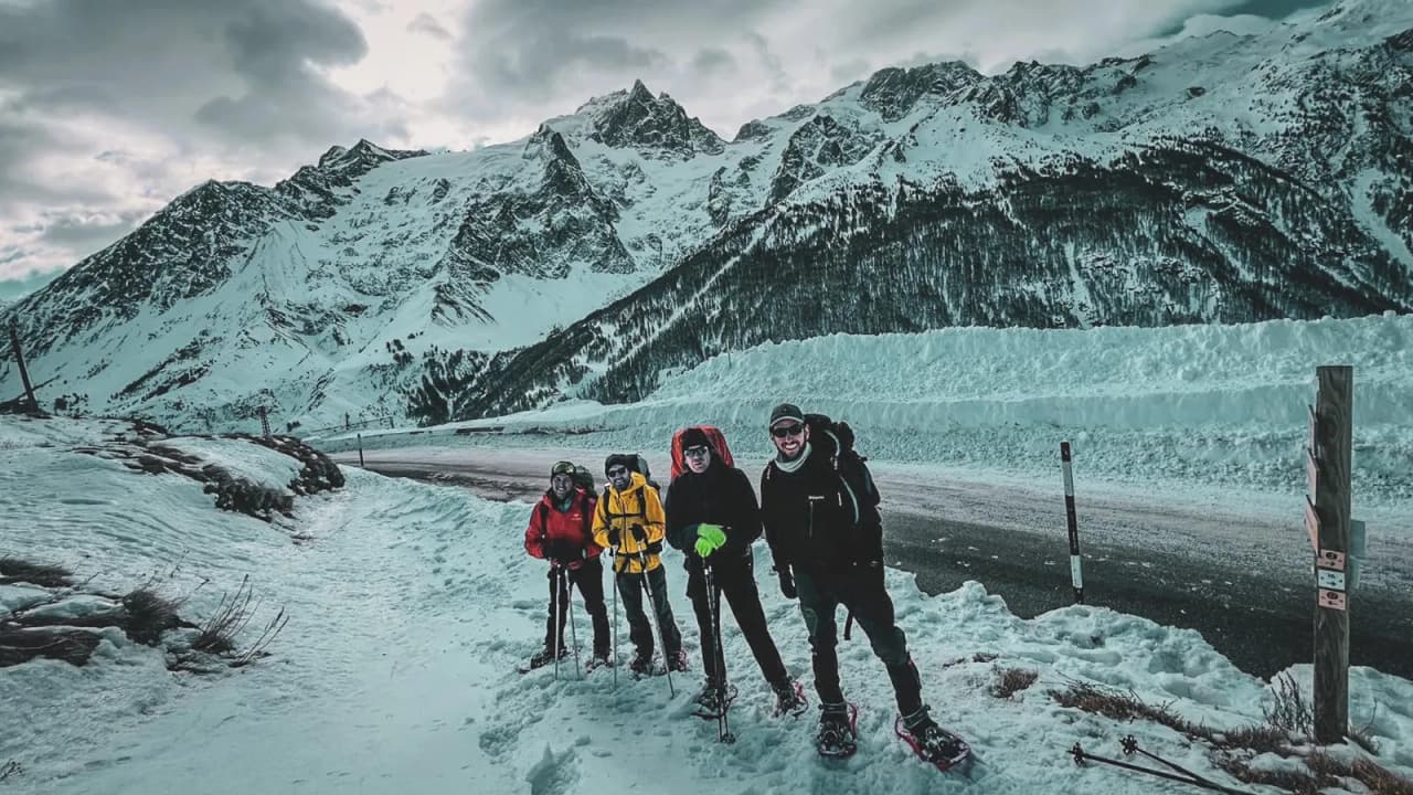Four adventurers on snowshoes pose in front of snow-capped mountains, ready for an expedition.