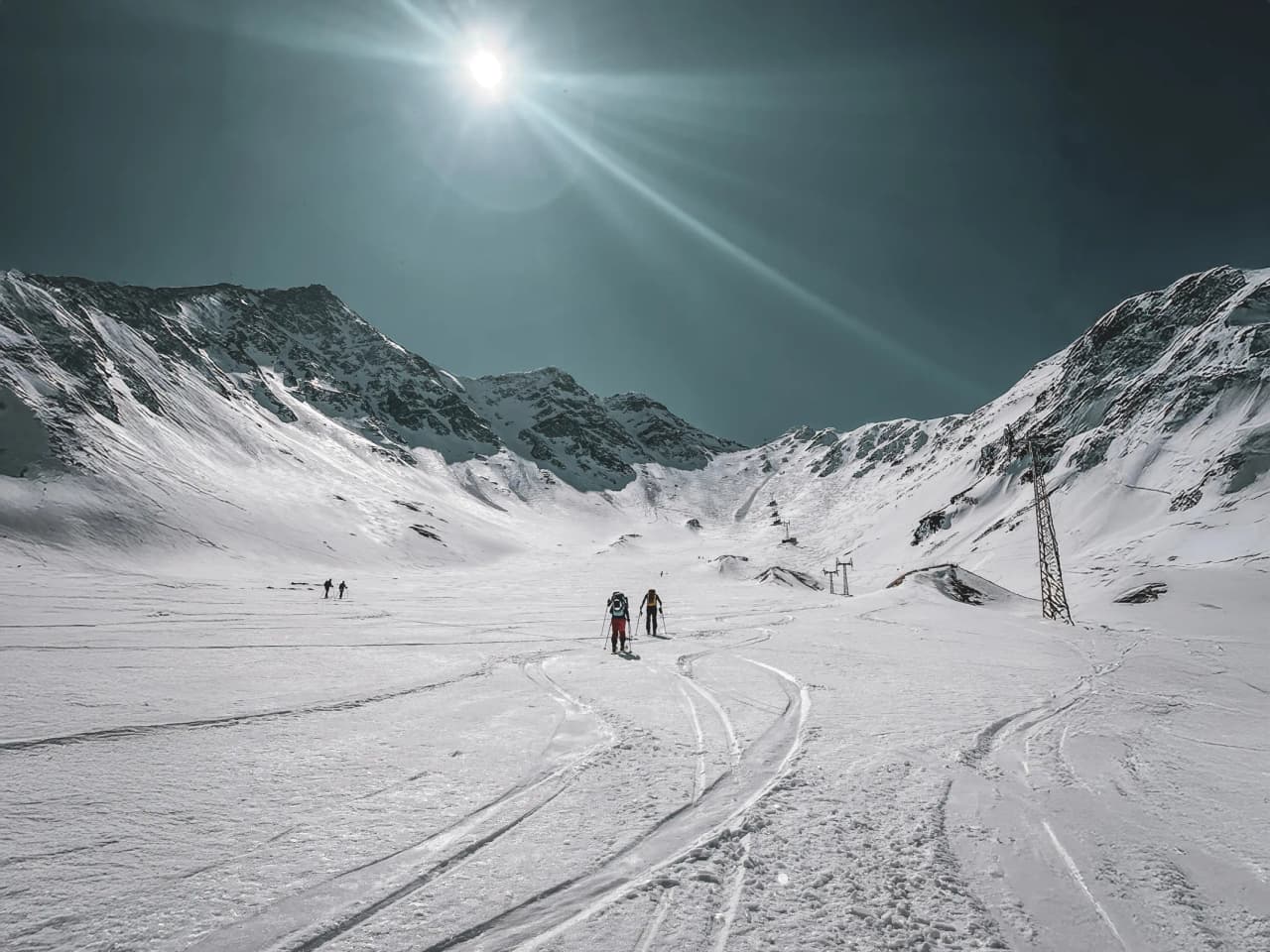 Two skiers venture out into a pristine Alpine landscape, in brilliant sunshine.