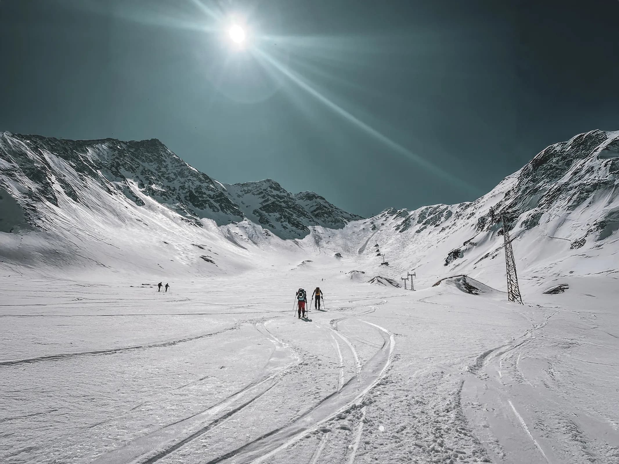 Two skiers venture out into a pristine Alpine landscape, in brilliant sunshine.