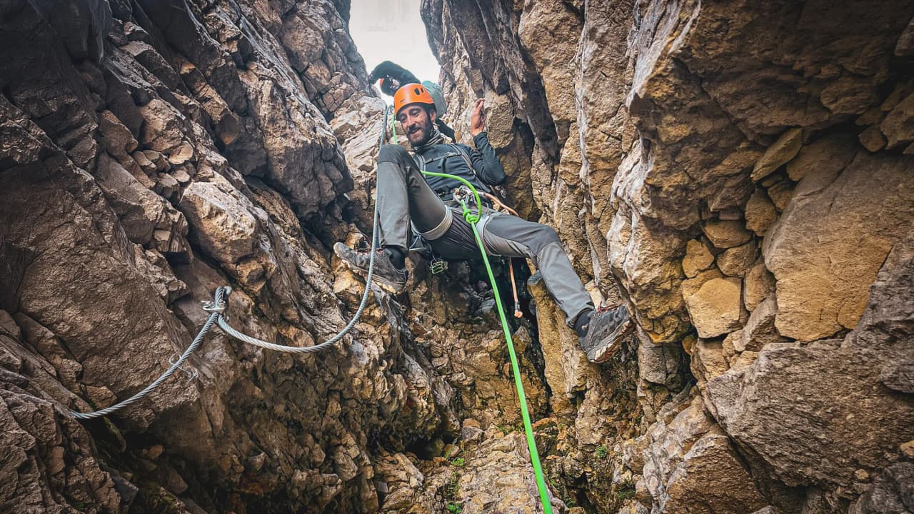 A fully kitted-out climber making his way through a narrow rocky passage on Mont Aiguille, surrounded by spectacular scenery.