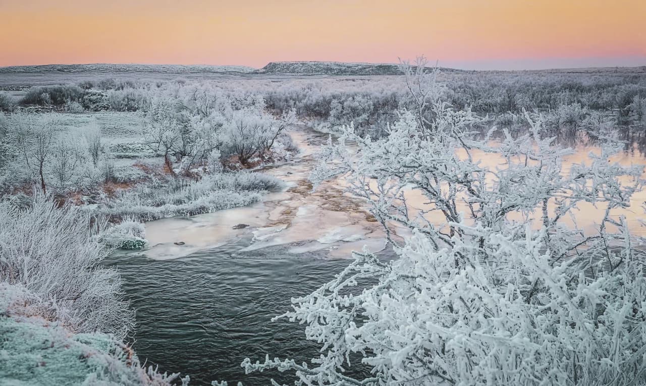 An enchanting winter landscape in Lapland, with frozen rivers, frosted trees and pastel skies.